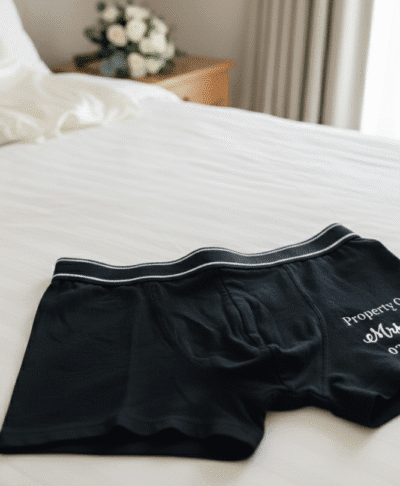 Groom's personalised boxer shorts laid out on a bed on the wedding morning. The black cotton boxer shorts feature custom text, making them a perfect groom gift or detail shot for wedding photography.