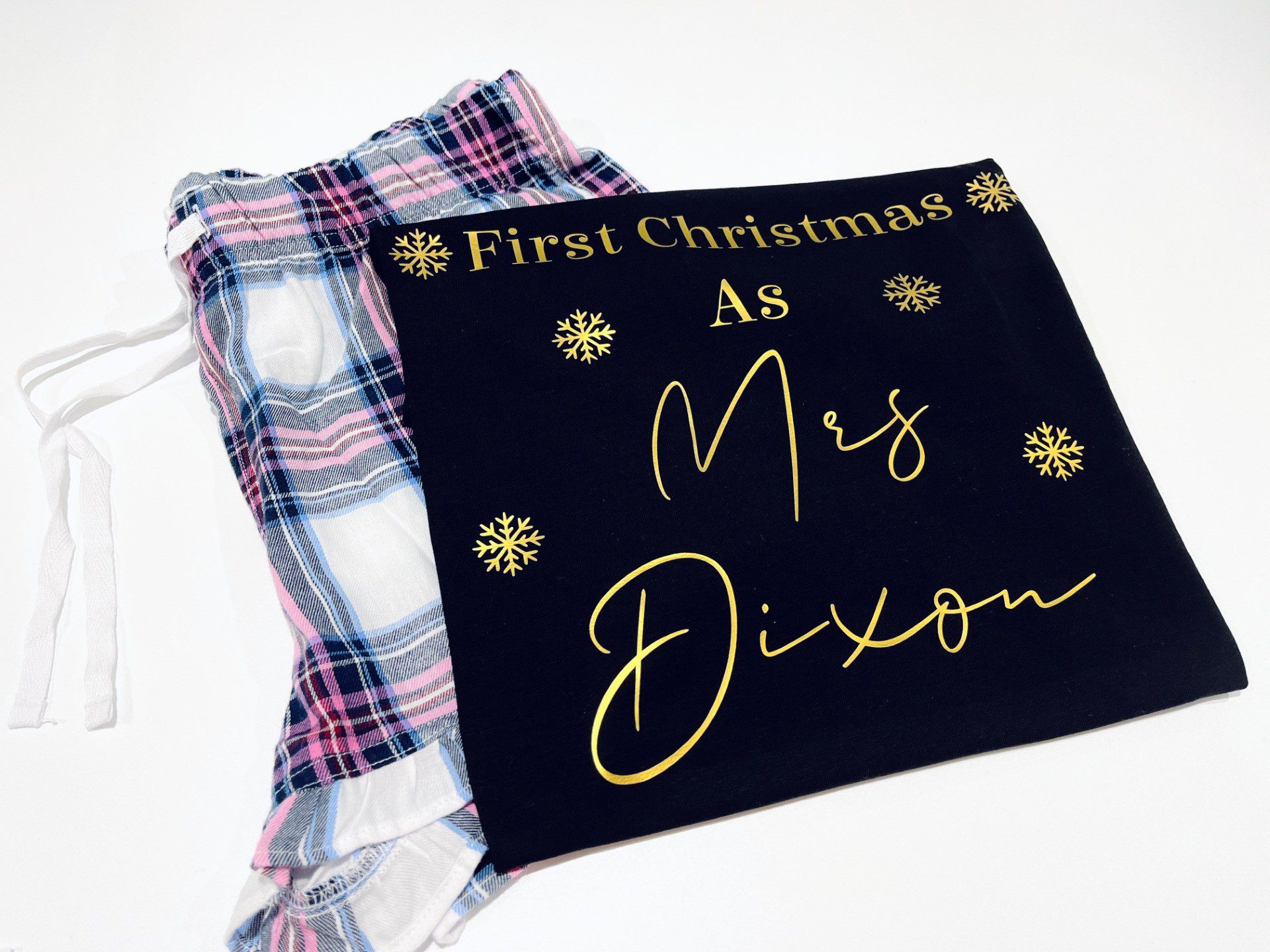 Personalised First Christmas short pyjamas with married name and gold snowflake design, folded with pink and blue check shorts – festive newlywed gift.