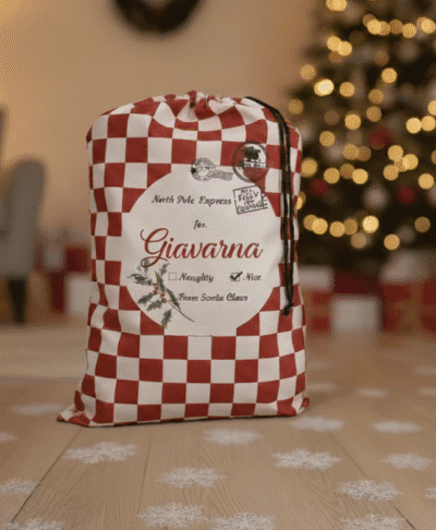 Luxury personalised Santa sacks for kids, featuring a red and white checkered North Pole Express bag with the name 'Giavarna'. Perfect Christmas morning setting on a hardwood floor with snow flake details, blurred Christmas tree lights, and cosy home decor.